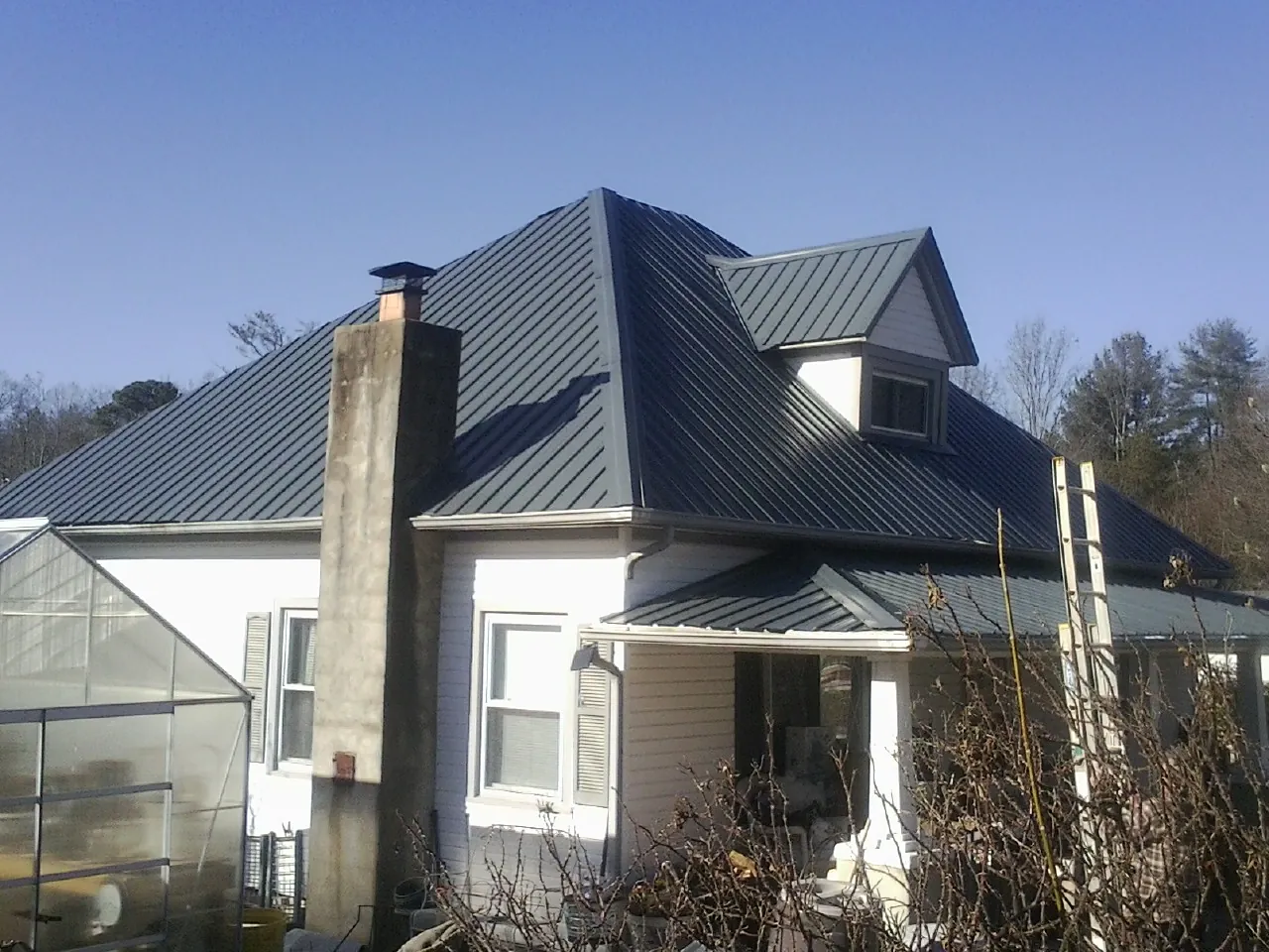 Dark blue standing seam metal roof on a white farmhouse with dormer — Slate & Tile Roof Repair by Roofing Brothers in Fort Shaw