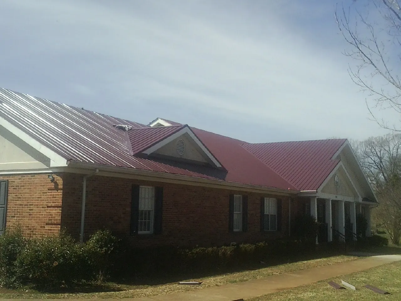 Red metal roof with gabled entries on a long brick building, from a Hail Damage Roof Repair job in Fort Shaw