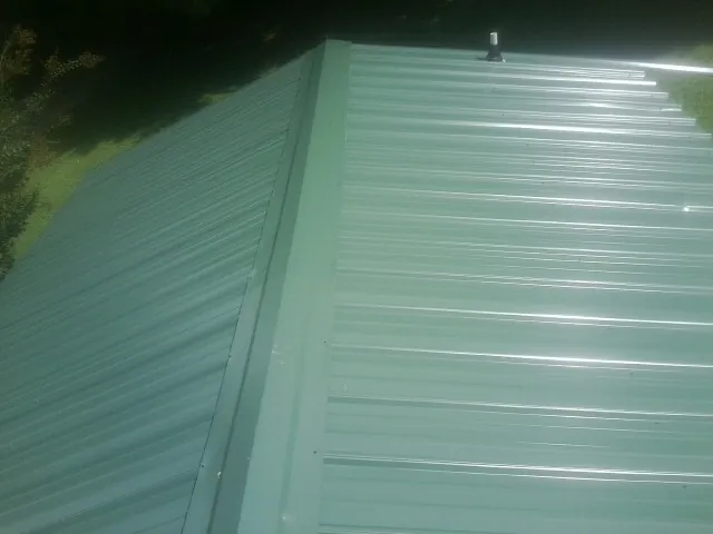 New green metal panels meeting at the ridge of a roof — Flat Roof Repair work by our crew in Fort Shaw