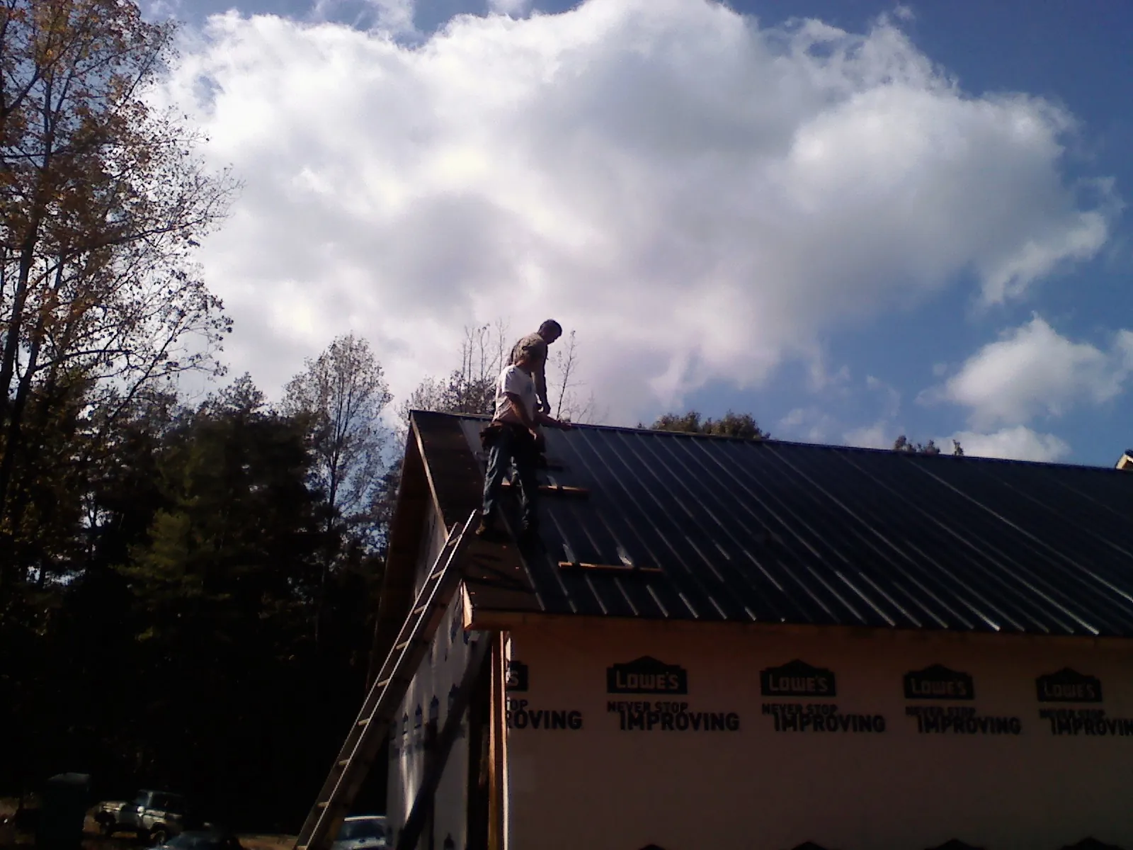 Roofer fastening dark metal panels high against a cloudy sky, from a Roof Inspection job in Fort Shaw