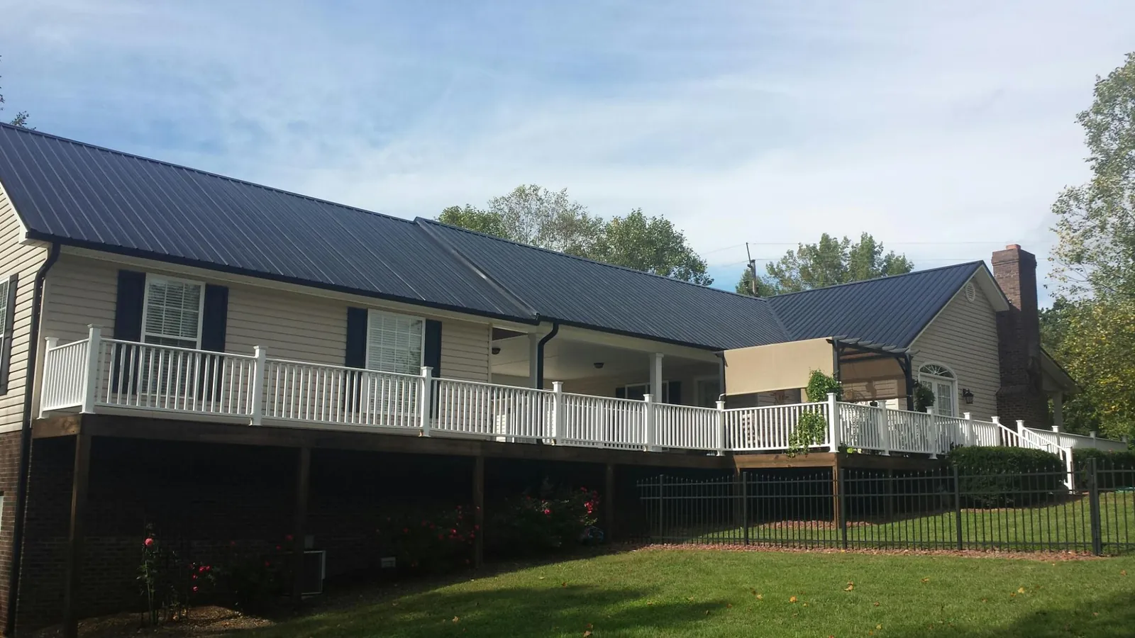 Black metal roof above a long white railed deck on a hillside home in Fort Shaw