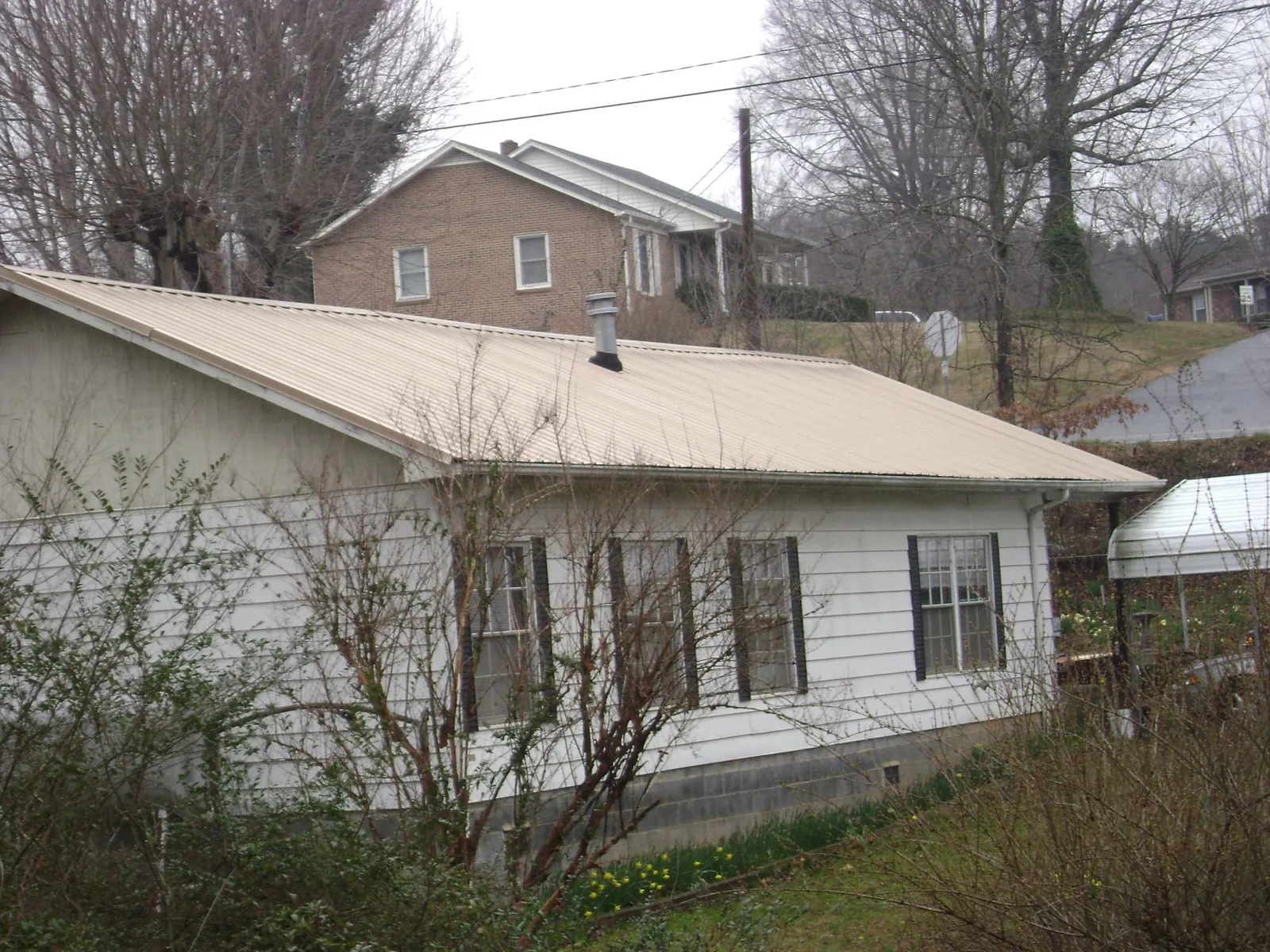 Tan metal roof on a white sided house set into a hillside — Commercial Roofing by Roofing Brothers in Fort Shaw