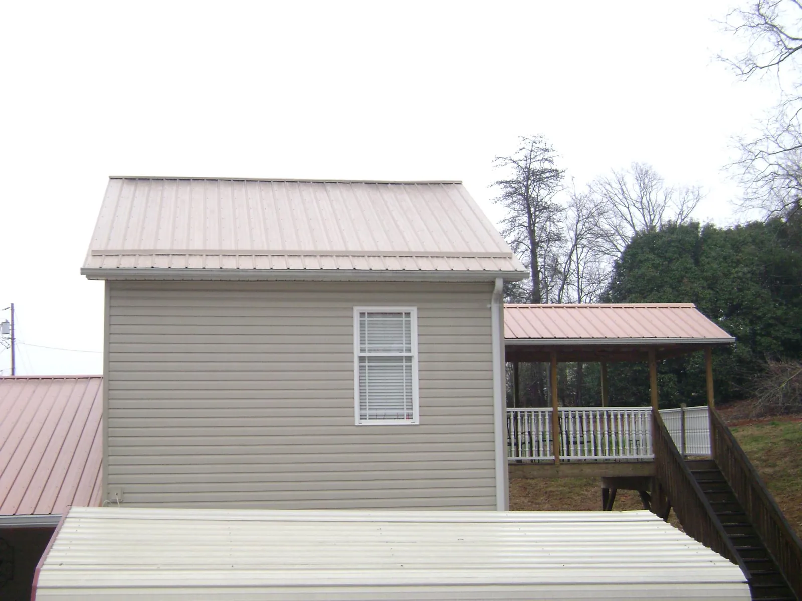 Tan metal roofs on a two story addition and attached porch, from a Roof Replacement job in Fort Shaw